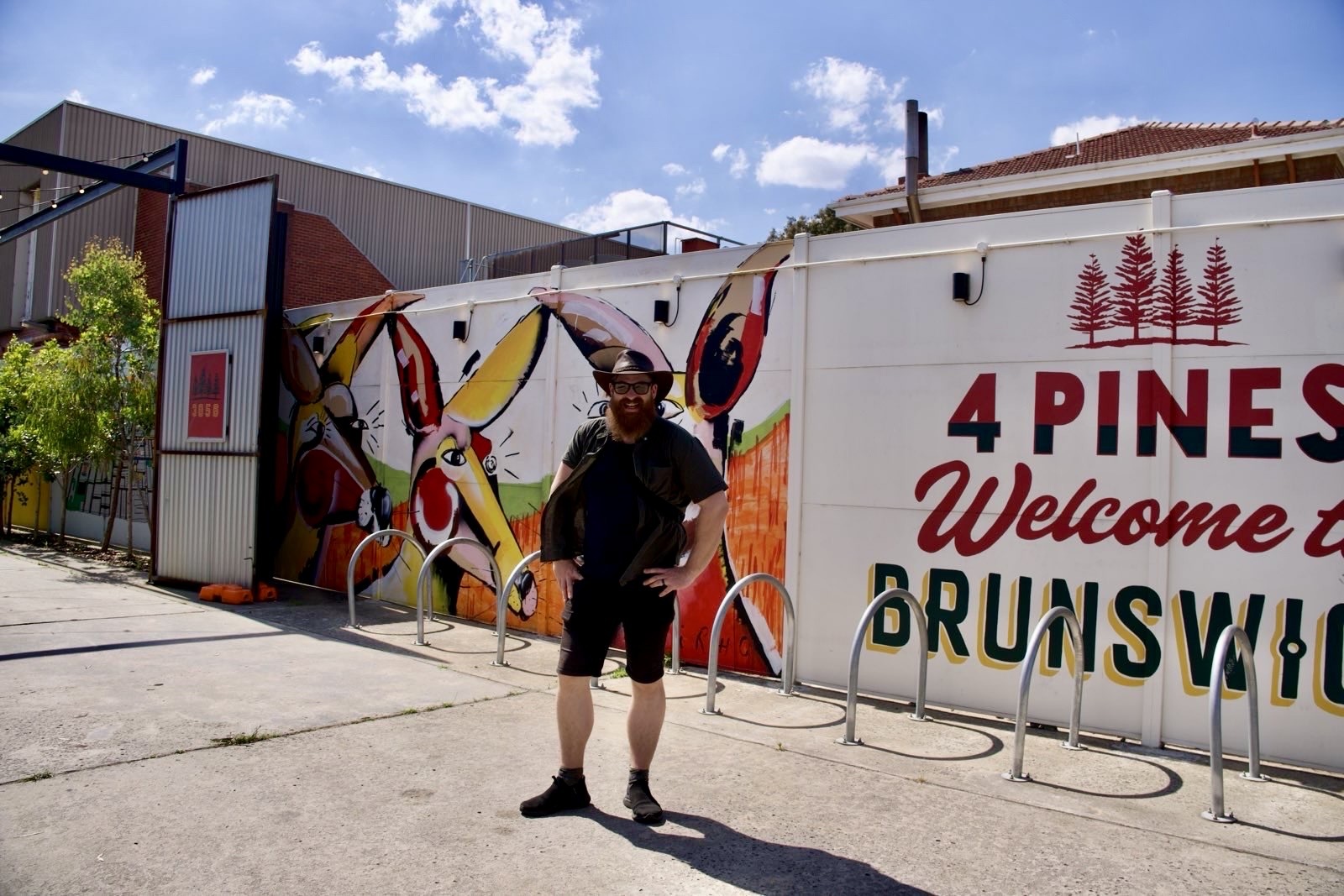 a man with an incredible beard in front of a sign that reads 4 pines welcome to brunswick